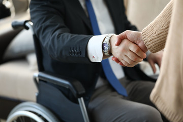 Close-up view of co-workers shaking hands. Businesswoman and disabled colleague on wheelchair. Business meeting and negotiations. Adaptation of people with disabilities in society concept