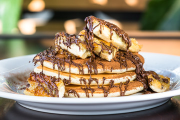 Pancakes are decorated with a banana and covered with chocolate syrup on a white plate. Bananas and chocolate. Close up