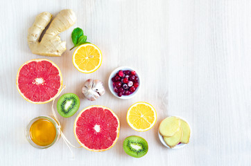 foods with vitamin C for Immunity boosting during the epidemic, colds. flat lay, top view on honey, ginger, lemon, kiwi, grapefruit, cranberries, garlic on light wooden background, copy space