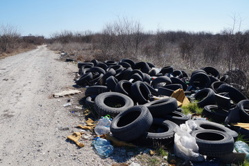 trash and old tires lie near a road in a field, pollution of nature
