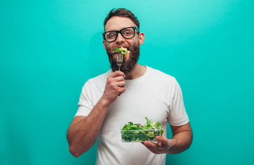 Happy healthy man eating salad wearing white t-shirt isolated over blue background. Healthy lifestyle concept
