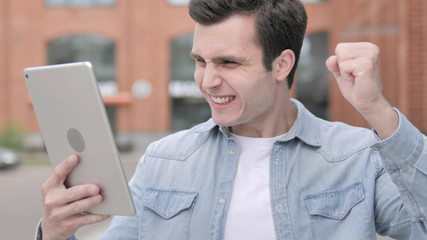 Man Standing Outdoor and Cheering for Success on Tablet