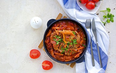 Ossobuco, beef shank stew on the bone with carrots, tomatoes and celery in a serving cast-iron frying pan on a light concrete background. Main dishes. Italian food.