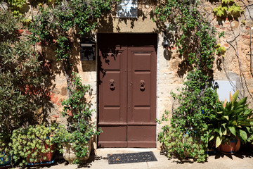 Fototapeta na wymiar Montemerano (GR), Italy - September 11, 2017: A house door with flowers in Montemerano village, Manciano, Grosseto, Tuscany, Italy, Europe
