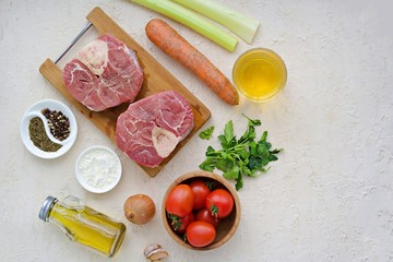 Ingredients for ossobuco, beef shank stew on a bone with carrots, tomatoes and celery on a light concrete background. Main meat dishes. Italian food. Copyspace. Top view.