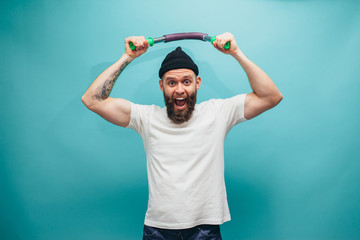 Naklejka premium Handsome bearded hipster guy exercising with expander. Crazy sports man emotions. Guy with beard wearing casual beanie and white t shirt.