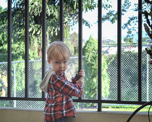 A little european boy child stands next to a lattice cell in quarantine sad. Closed school...
