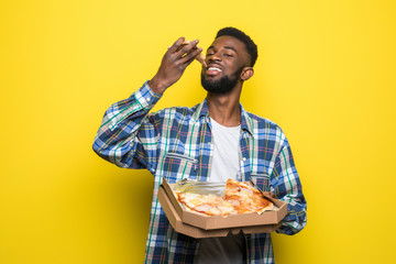 Afro american man eating slice of pizza over isolated yellow background