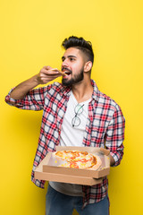Handsome indian man eating tasty pizza on yellow background