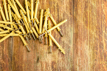 Pile of plastic dowels with metal screws lie in a row on a scratched wooden table. Home repair concept. Copy space for text.