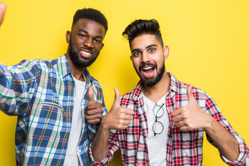 Portrait of a two mixed race men taking a selfie while standing together isolated over yellow...