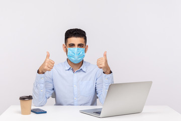 Fototapeta na wymiar Male employee in hygienic face mask sitting in office and showing thumbs up, using excellent protect filter against contagious disease coronavirus, 2019-nCoV, flu epidemic. studio shot, isolated