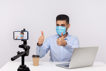 Man in medical mask gesturing thumbs up making video about flu recovery, coronavirus infection,...
