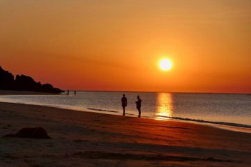 Sunset with orange sky at Nacpan beach with two girls and sleeping dog, El Nido, Palawan, Philippines