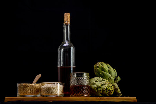 Arroz, quinoa y cuscus con alcachofas, botella y vaso de vino sobre tabla de mader y fondo negroa 