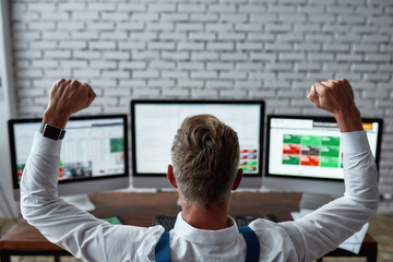 For the true difference. Rear view of middle-aged trader raising his hands while sitting in front of pc and analyzing stock market chart. Businessman working in the office.