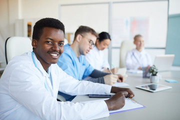 Fototapeta premium Portrait of young African-American doctor smiling at camera during medical council or conference in clinic, copy space