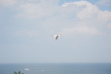 Fototapeta na wymiar A white drone, a quadrocopter with a camera flies against a blue sky and sea. Photography, concept.