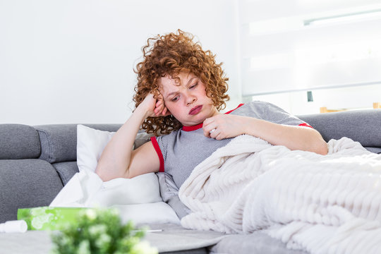 Weak woman, wearing casual clothes is sitting on a sofa and taking a pill. Sick day at home. Young woman has common cold. Sickness, seasonal virus problem concept.