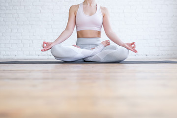 Unknown young caucasian woman sits in lotus and mudra position In a bright spacious sports hall on yoga mat. Concept of pacification spirituality and healthy lifestyle