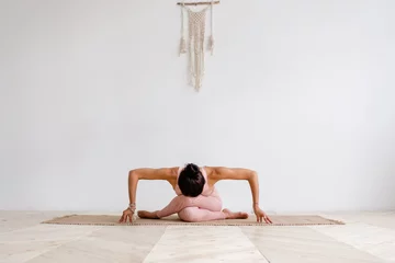 Fotobehang Yogaschool Jonge aantrekkelijke vrouw die yoga beoefent in heldere yogales op houten vintage vloer, zittend in variatie van Gomukasana-oefening met voorwaartse buiging, Cow Face pose, trainen, roze sportkleding dragen