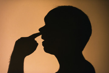 Shadow silhouette on a wall of a profile of a man picking his nose