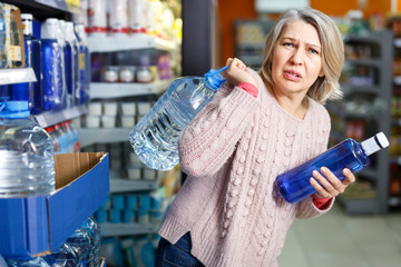 Tense adult woman lifting heavy bottle water