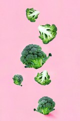 Falling soaring green broccoli slices on a pink background. Concept of flying food, green vegetables, diet food, veggies pattern, food blog. Vertical with Copy space for text.