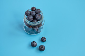Glass jar with blueberries on a blue background.