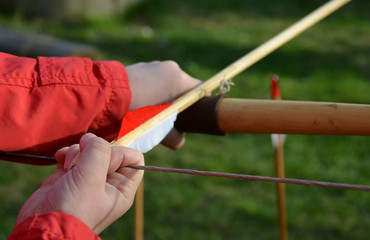 little boy stands with a bow and stretches a bowstring with an arrow made of wood with a feather...