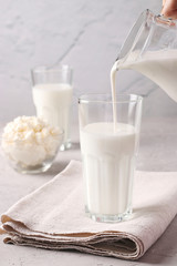 Kefir or Ayran fermented drink is poured into a glass from a jug, as well as cottage cheese in a bowl on a light gray background, Close up