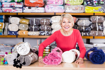 friendly senior seller showing wide assortment of home textiles