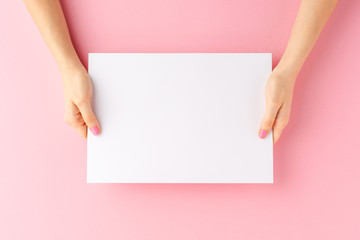 Young woman’s hands holding blank paper sheet on pink background. Mockup