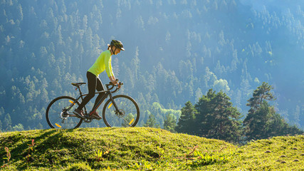 A young smiling woman on a cyclocross bike rides against the background of a green forest on a...