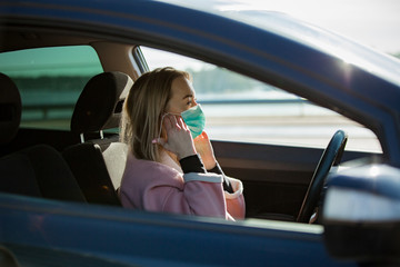 Woman in protective mask driving a car on road. Safe traveling.