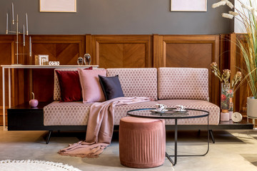 Stylish interior of living room with design pink sofa, elegant pouf, coffee table, plants, pillows, decoration, elegant personal accessories and mock up poster frames in modern home decor. 