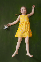 Girl in a yellow dress with a watering can in hand lies on a green background