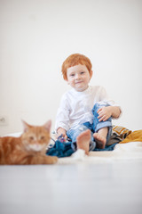 Funny red-haired boy in white bed with a red cat