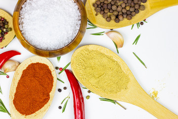 Top view of variety of spices and seasonings (indian curry, different pepper, paprika powder, salt, dry ginger and curcuma) for cooking in wooden spoons on white kitchen table background.