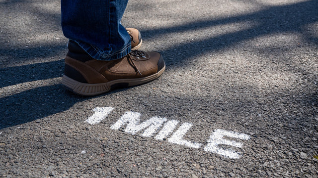 1 Mile Marker On A Paved Hiking Trail With A Man Wearing Hiking Boots.