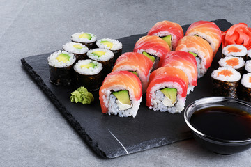 Sushi maki with salmon and avocado, sushi philadelphia, soy sauce and ginger on a background of slate board. © vitals