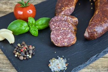 Smoked salami homemade with spices on a slate plate on a rustic wooden background