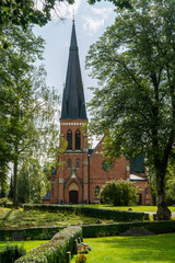 Fototapeta na wymiar Beautiful brick church with a tall tower in a lush green environment