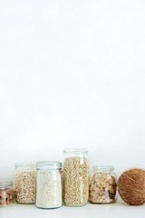 Various raw cereals, grains, oatmeal in glass jars and coconut on a light background. Zero waste concept, food storage in the kitchen, healthy eating. Vertical with Copy space for text.