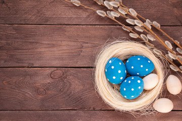 Easter holiday card. Classic blue painted eggs lie in a wicker nest and a pussy-willow branch on a dark wooden background. Copy space for text.