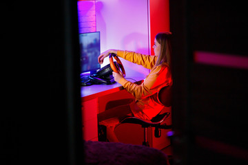 girl gamer playing racing on a computer. She uses a steering wheel. emotional play