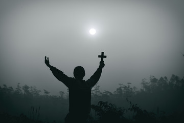 human kneeling down and raise the cross on the head for praying and worship God at morning. christian silhouette concept.