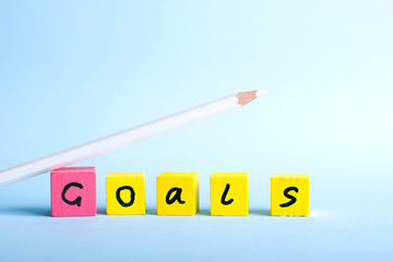 Colorful wood cubes and a white pencil on blue background. Goals concept.