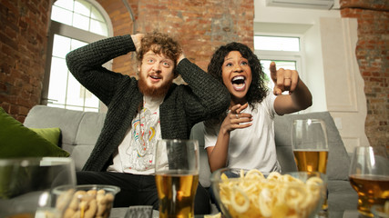 Fantastic. Excited couple, friends watching sport match, chsmpionship at home. Multiethnic friends, fans cheering for favourite national basketball, tennis, soccer, hockey team. Concept of emotions.
