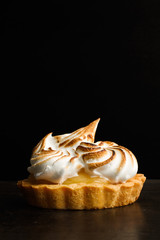 Lemon Pie con merengue sobre una mesa rústica y fondo negro aislado. Vista de frente. Copy space